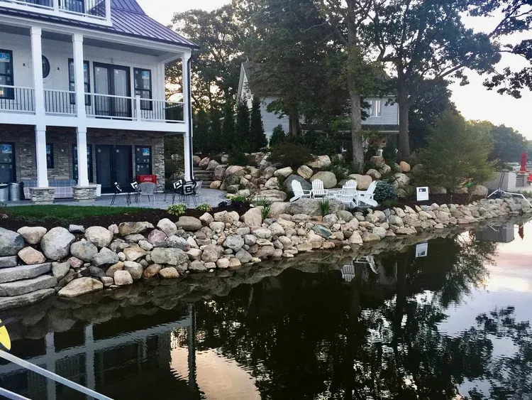 Lakeside house with stone retaining wall and calm water reflecting trees and building