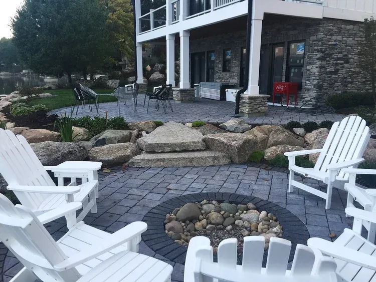 Patio with white Adirondack chairs around a stone fire pit beside a modern building
