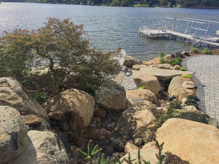 Rocky lakeside garden with shrubs and a dock extending into calm water