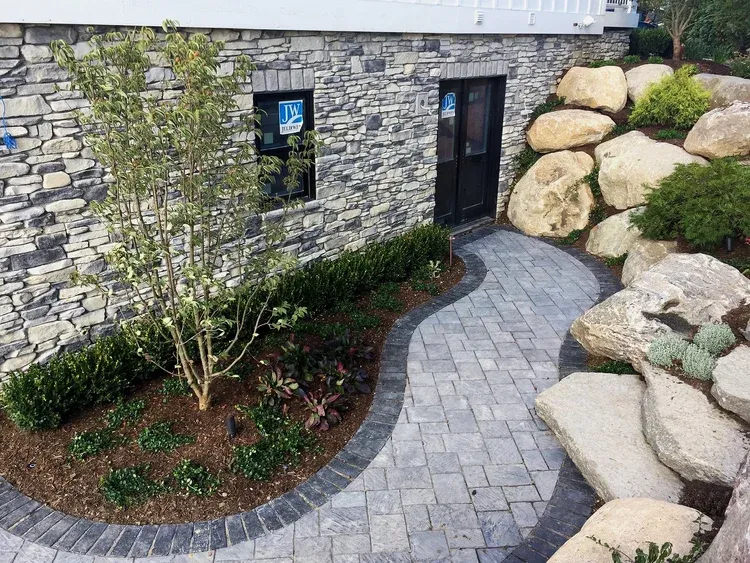 Stone building entrance with curved paver path, landscaped bed, and large boulders alongside the walkway