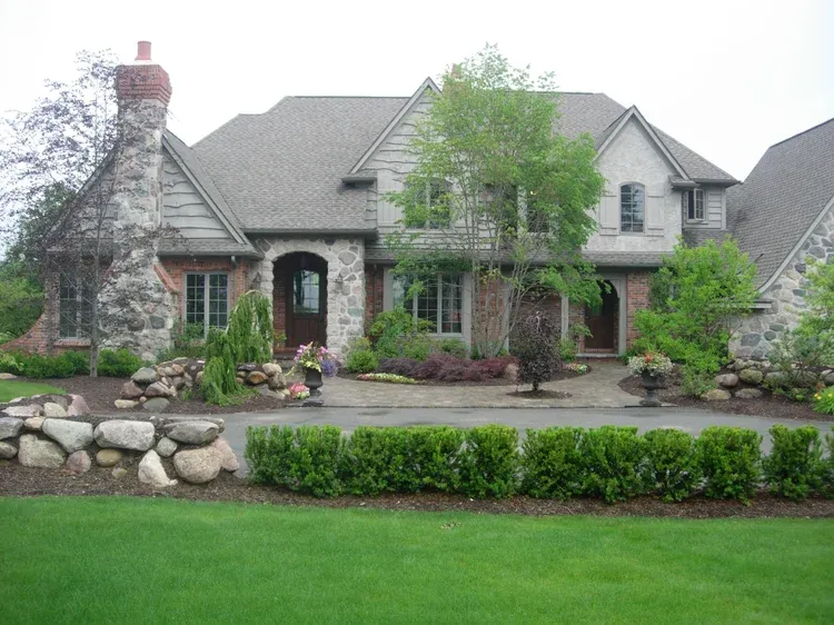 Stone suburban house with landscaped front yard, green lawn, and flower beds