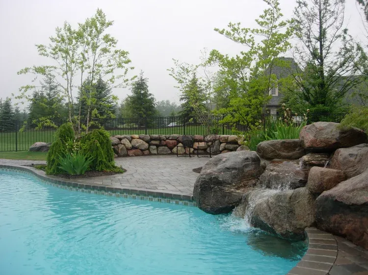 Backyard pool with turquoise water, stone waterfall, and lush green landscaping