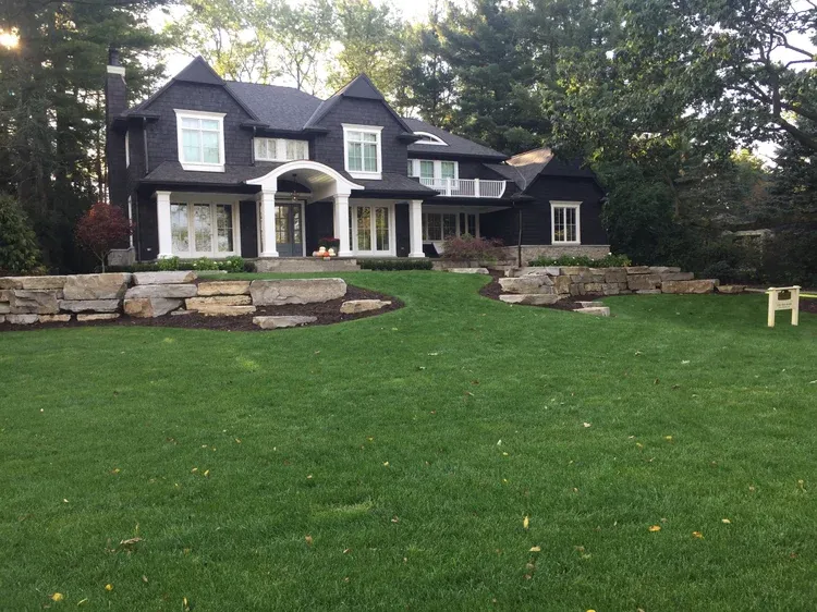 Large dark house with white trim, stone retaining wall, and a broad green lawn in front