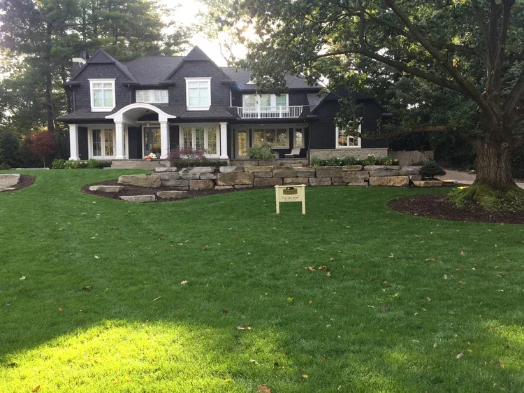Large house with white columns and a manicured green lawn in front, under tall trees