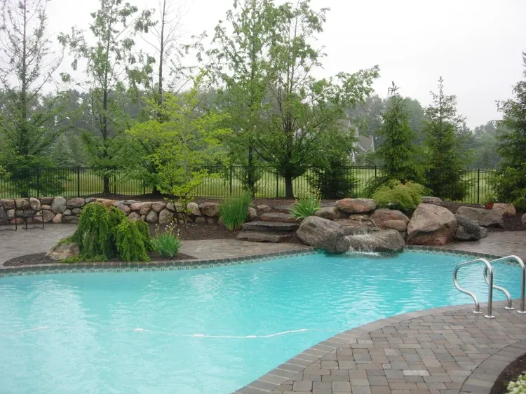 Outdoor swimming pool with turquoise water, stone edge, rocks, and green trees in the background
