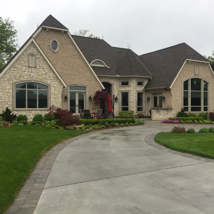 Large tan brick suburban house with arched windows and a curved concrete driveway