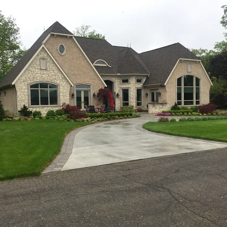 Large stone suburban house with a curved concrete driveway and manicured lawn