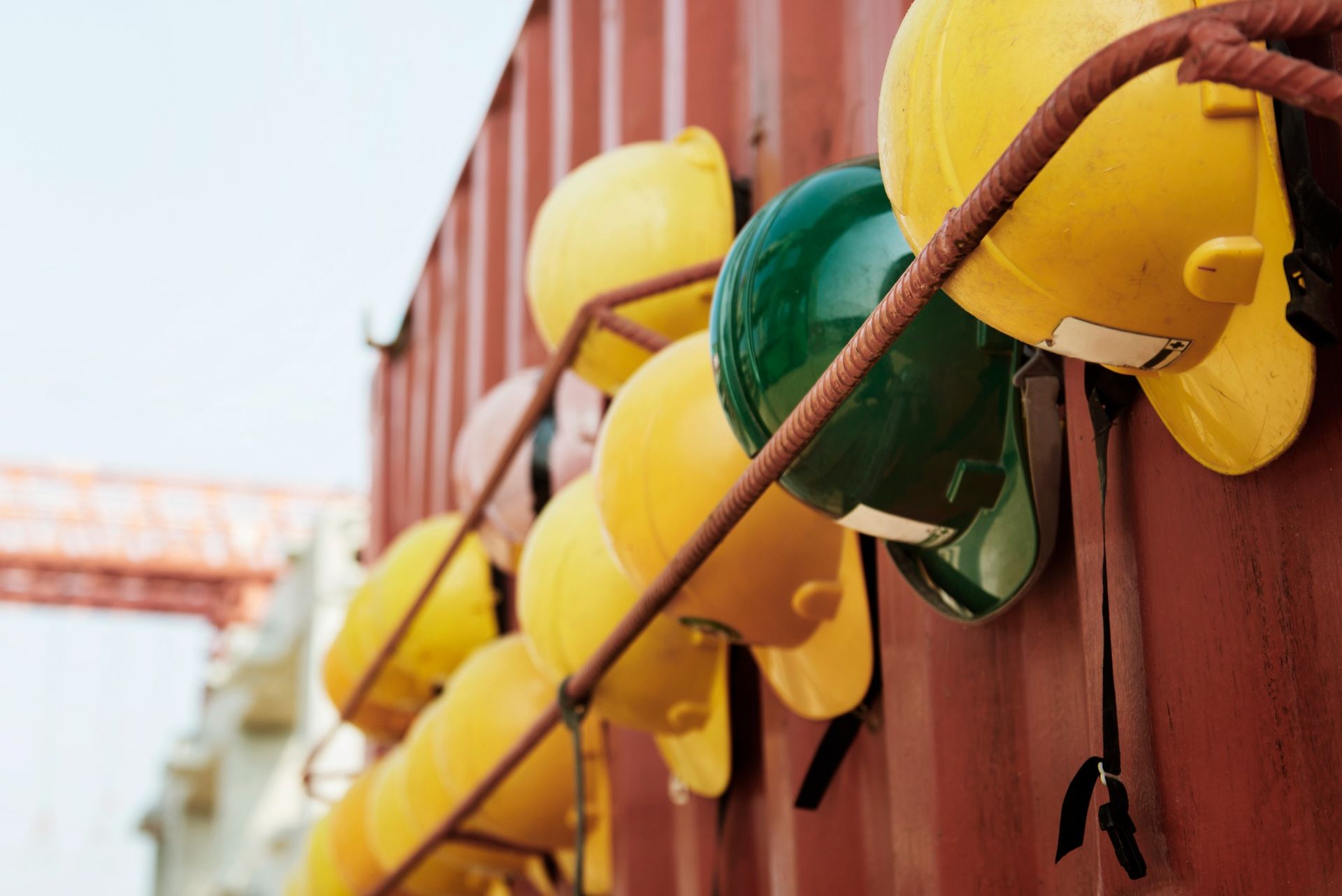 Row of yellow and one green hard hats hanging on a metal rack attached to a red container.