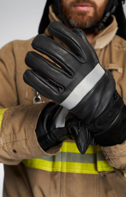 Bombero ajustándose un guante negro sobre una chaqueta de bombero color canela con franja reflectante.