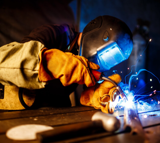 Un soldador con equipo de protección realiza soldadura de metal con una luz azul brillante en un taller.