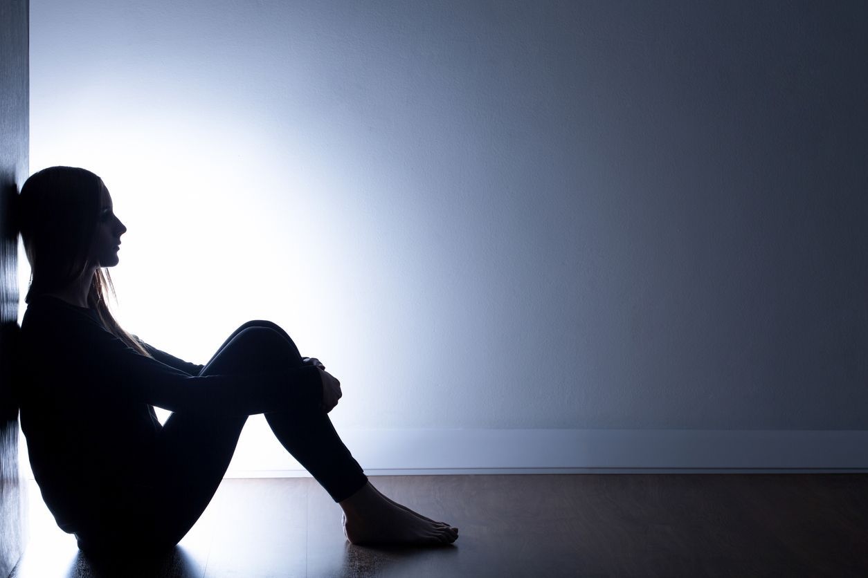 A teenager is sitting on the floor leaning against a wall.