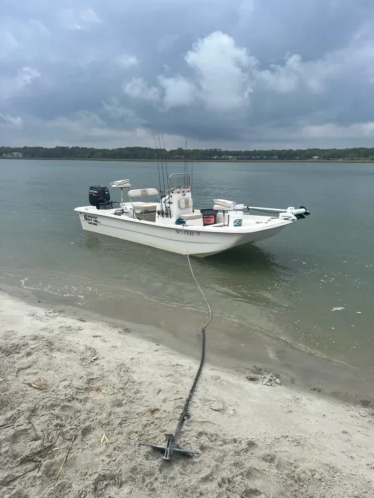 White fishing boat anchored on a sandy beach, under a cloudy sky.