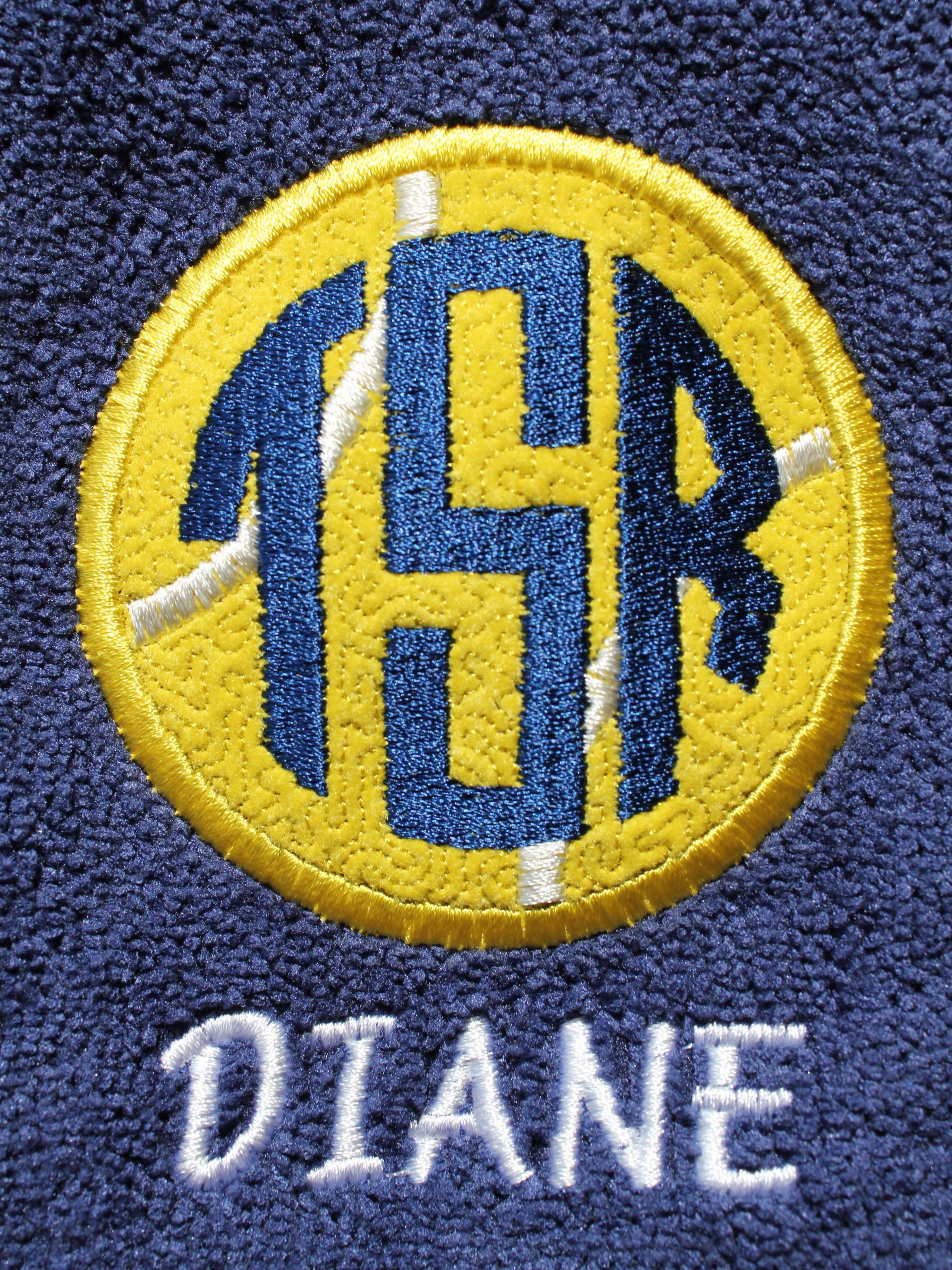 A navy blue fabric embroidered with a circular yellow patch featuring the dark blue monogram A navy blue fabric embroidered with a circular yellow patch featuring the dark blue monogram