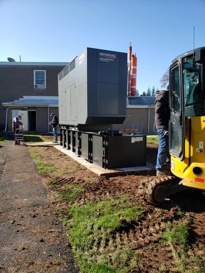 Large gray industrial unit being installed outside a building, with workers and a yellow excavator nearby.