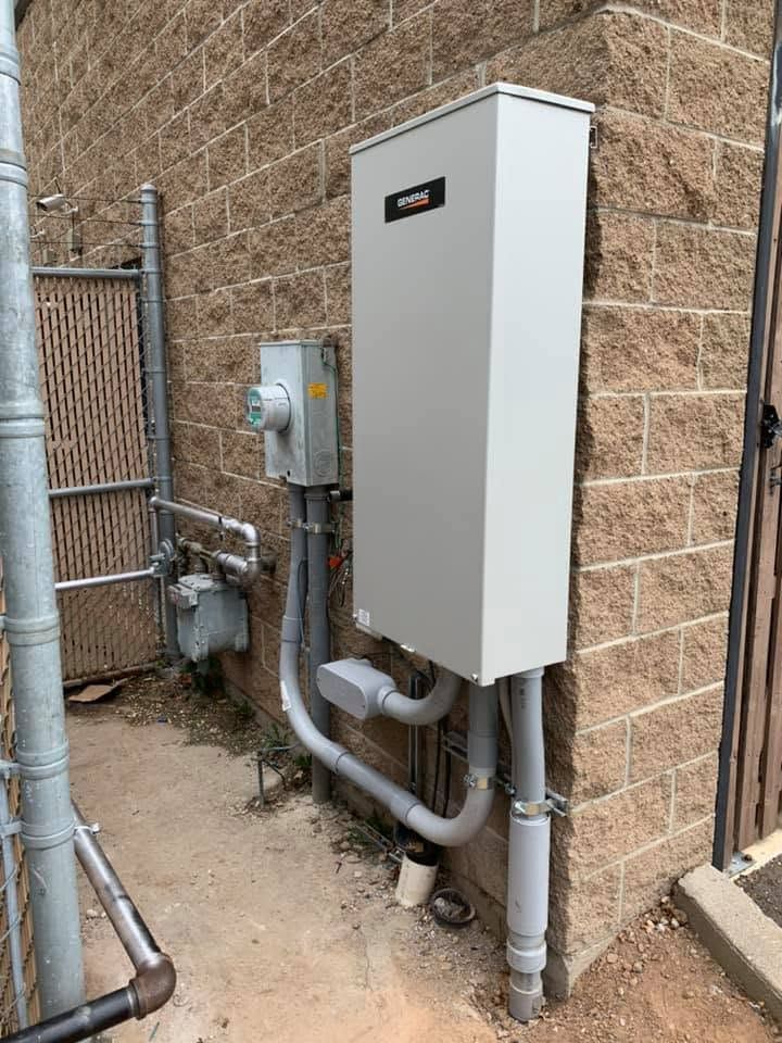 Outdoor utility panel and gas meter mounted beside a brick building with pipes and conduit