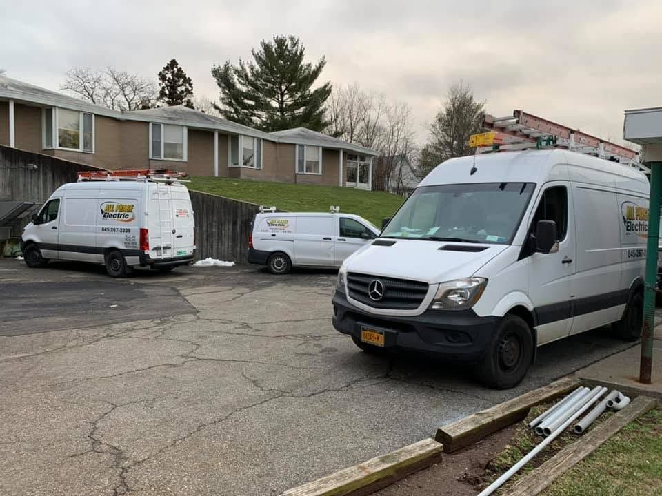 Three white service vans parked on a residential street in front of townhouses.