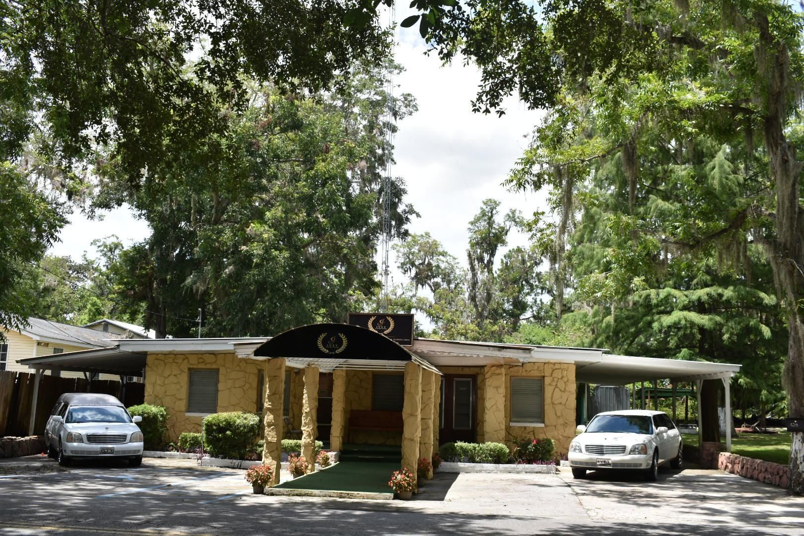 Low building with trees overhead and two parked cars in front
