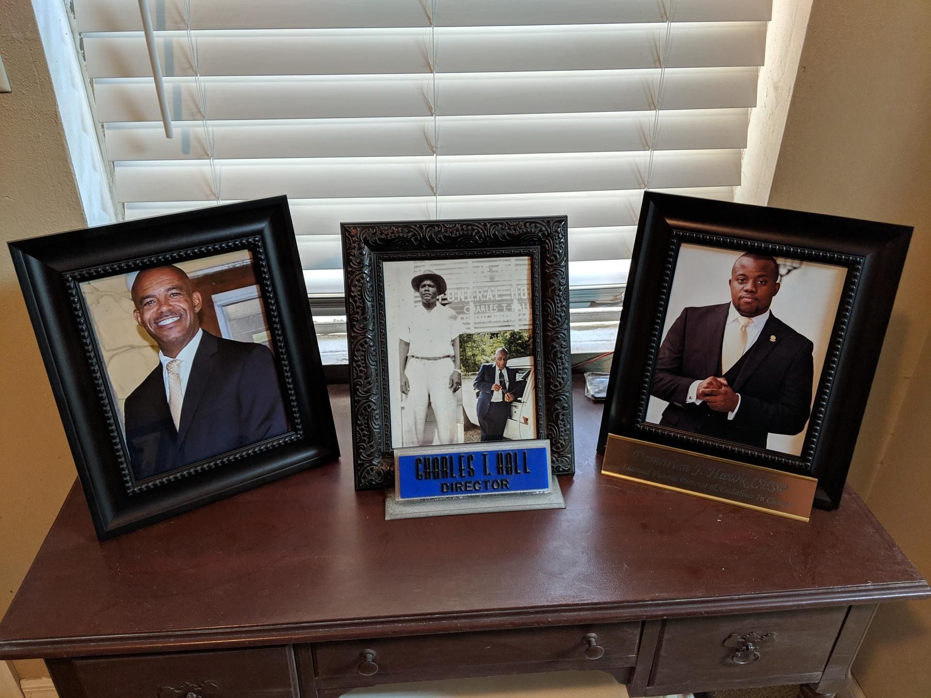 Three framed photos on a wooden table in front of white window blinds.