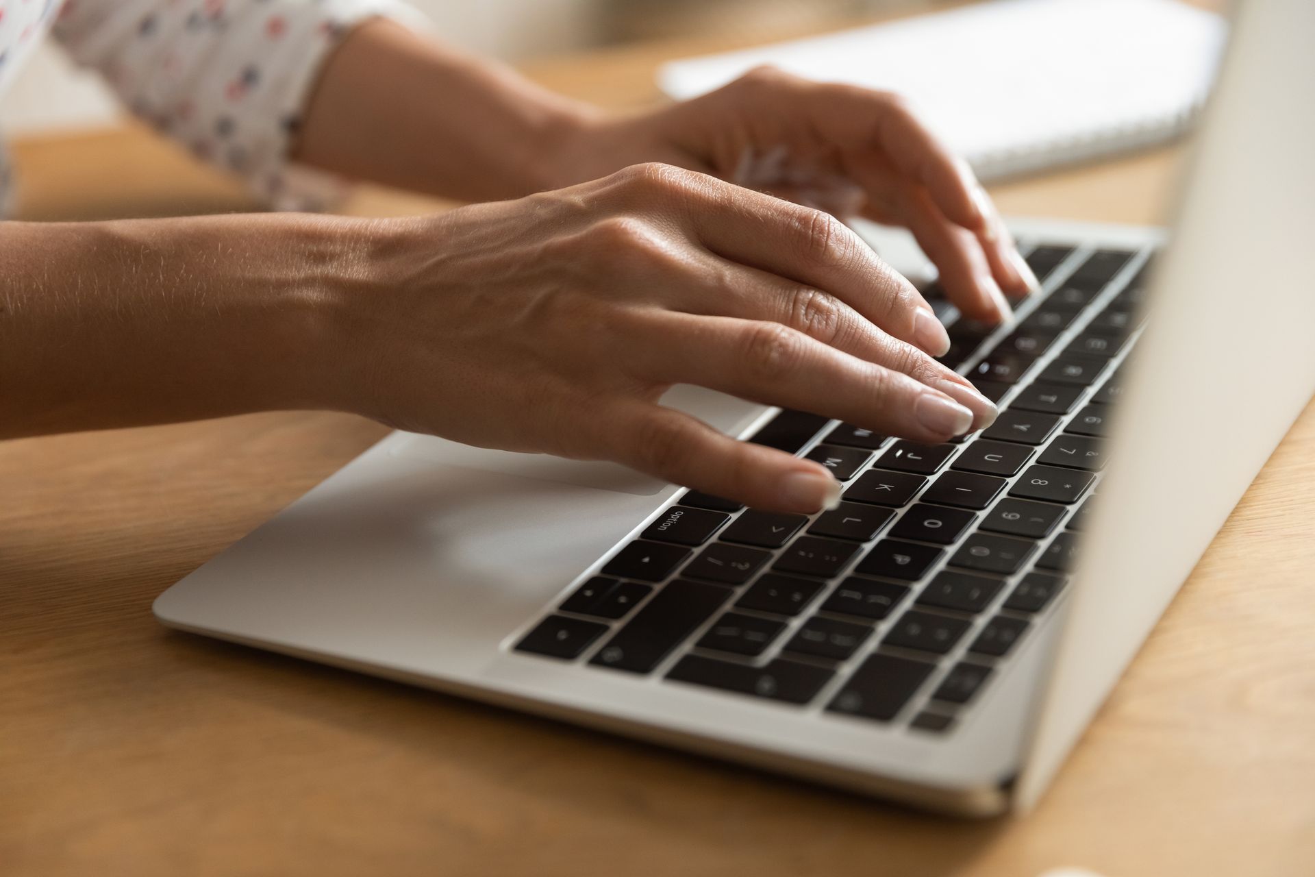Hands typing on a silver laptop keyboard at a wooden desk