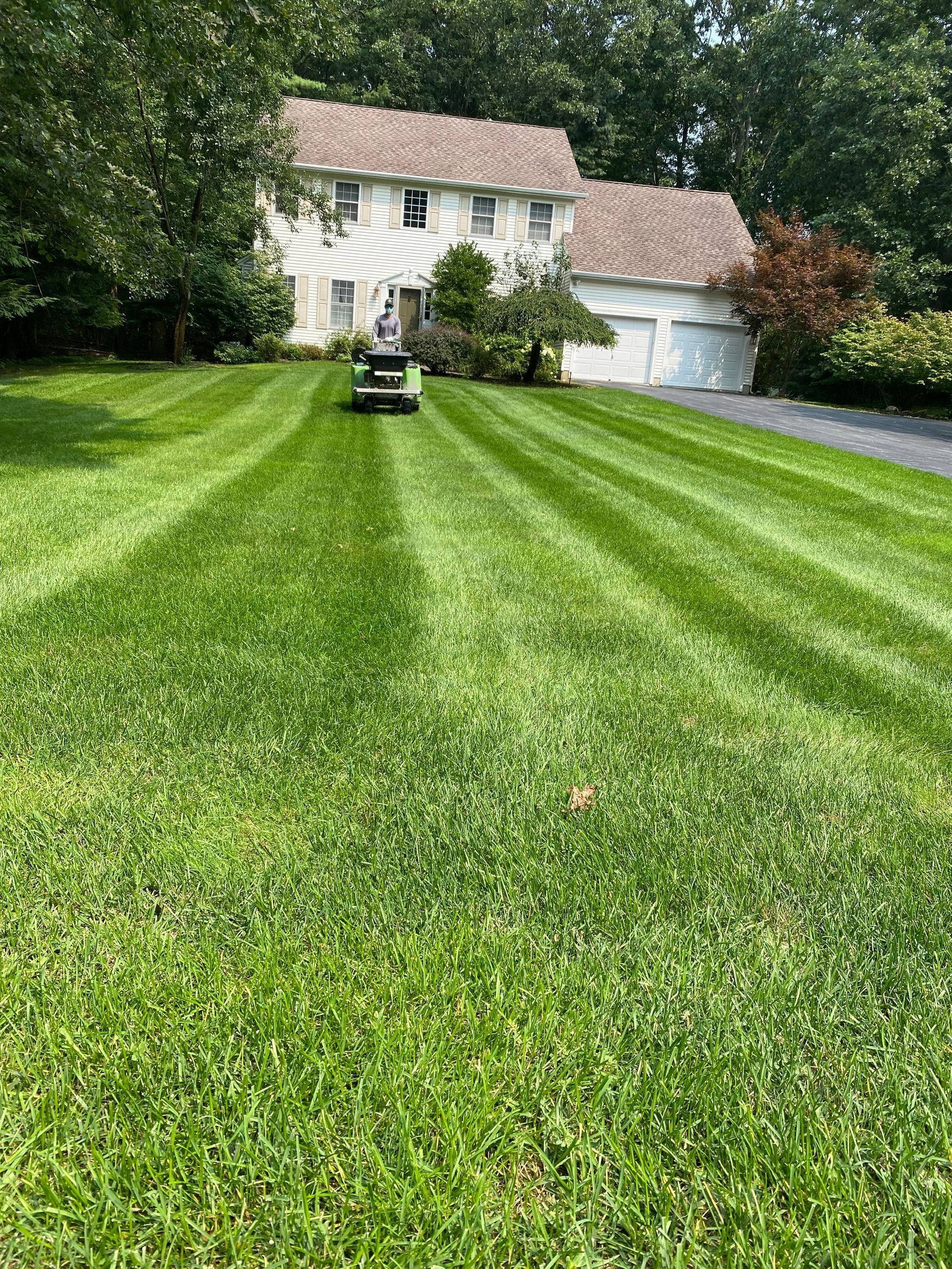A lawn mower is cutting a lush green lawn in front of a house.