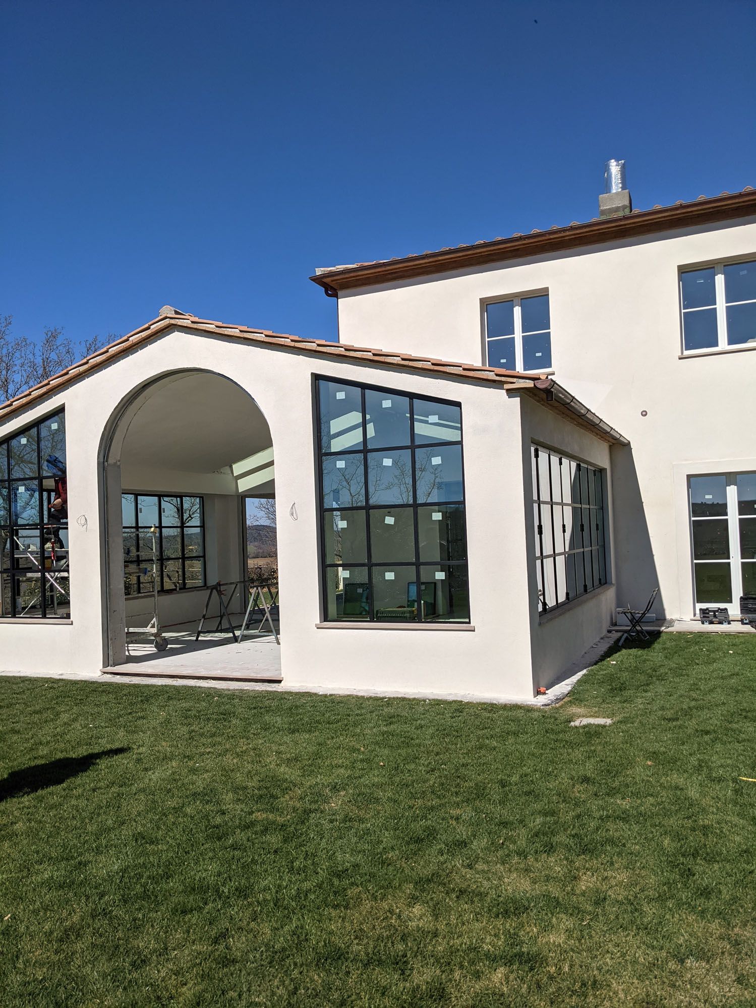 Esterno di una casa bianca con veranda, finestre con cornice nera, tetto di tegole rosse e prato verde sotto un cielo azzurro.
