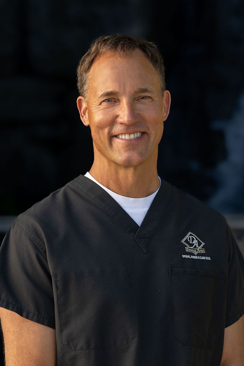 Dentist Dr. Opdhal in a black scrub top is smiling for the camera.