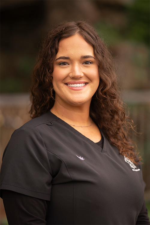 A woman in a black scrub top is smiling for the camera.