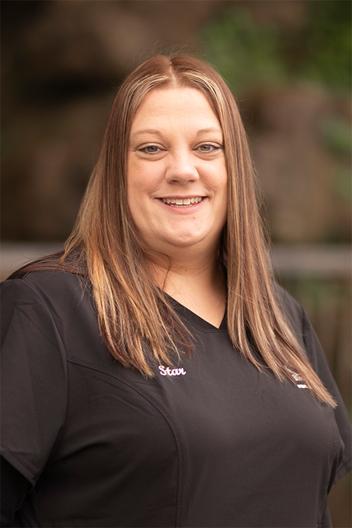 A woman in a black scrub top is smiling for the camera.
