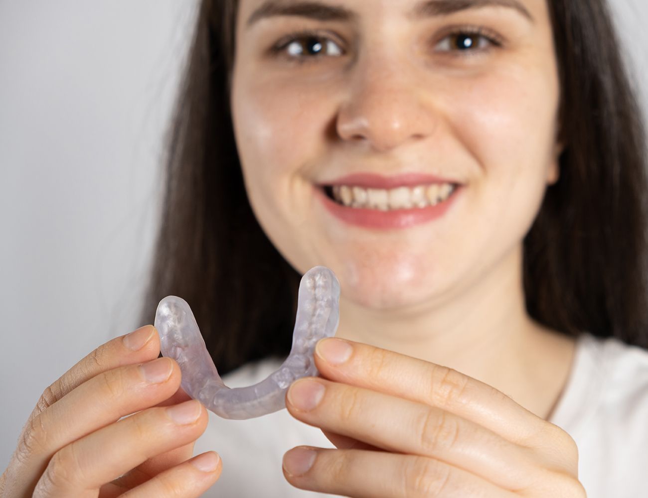 A woman is holding a clear mouth guard in her hands.