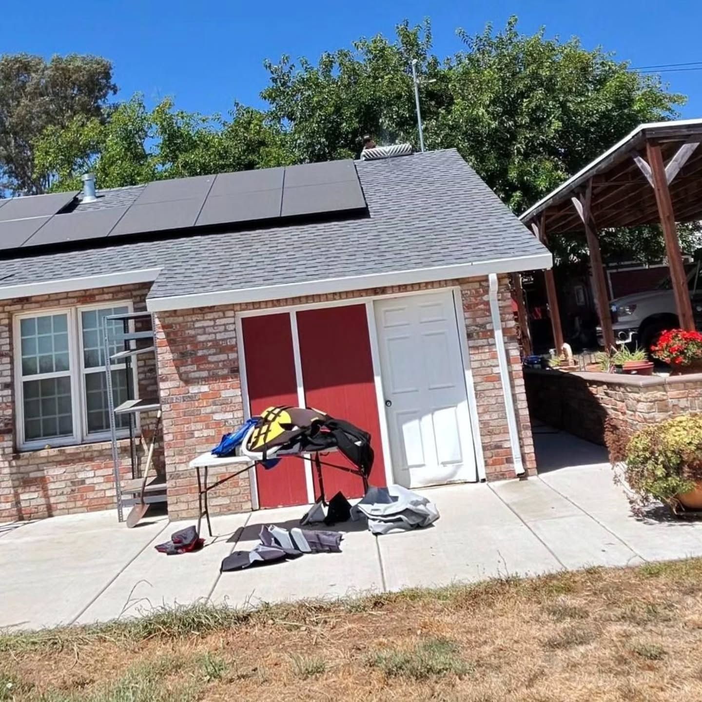 Brick house patio with solar panels, red and white doors, and a folding table with items on the sidewalk