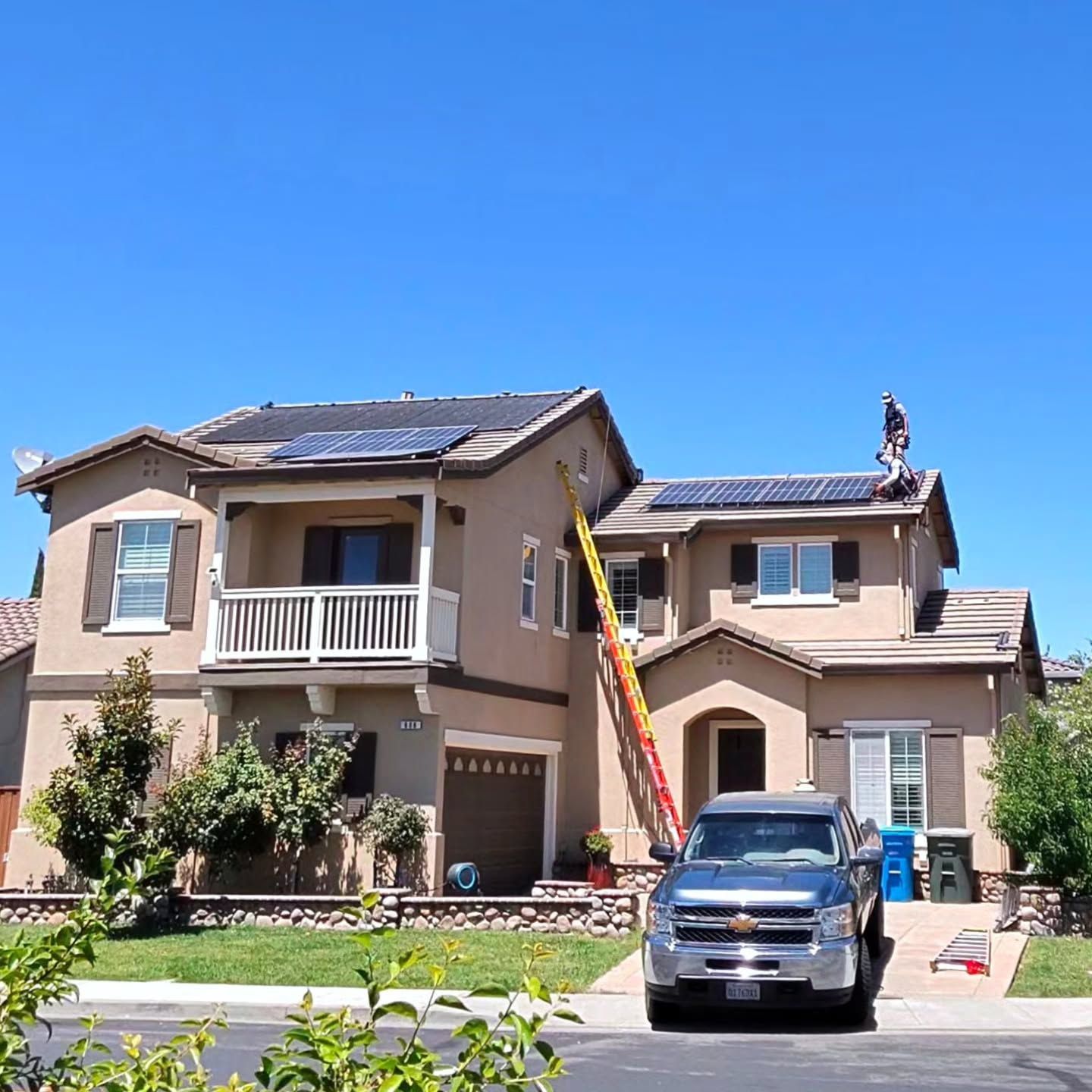 Two-story beige house with a blue truck parked in the driveway under a clear sky