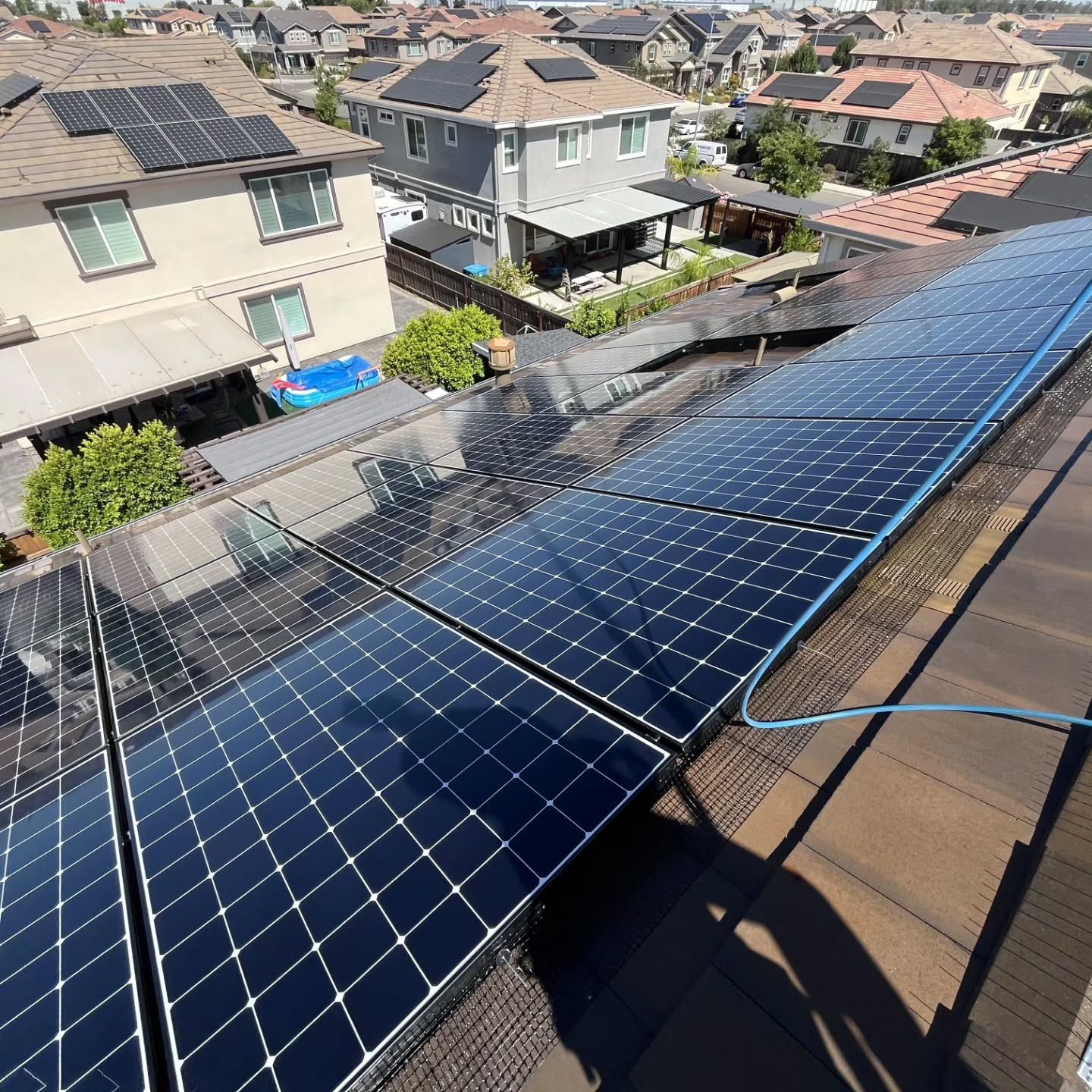 Rows of blue solar panels on a rooftop in a suburban neighborhood under bright sunlight