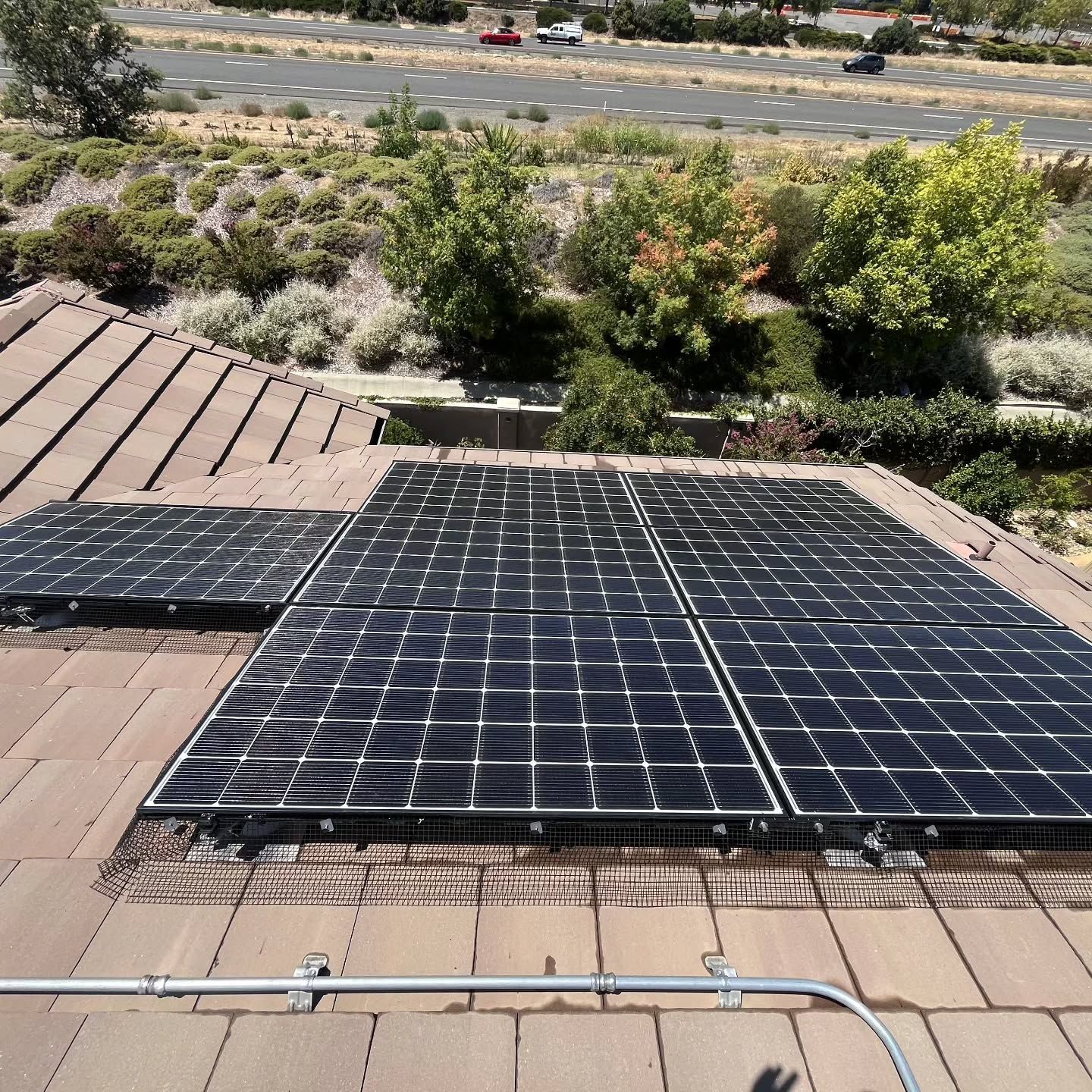 Solar panels mounted on a tiled rooftop with desert landscaping and a road in the background