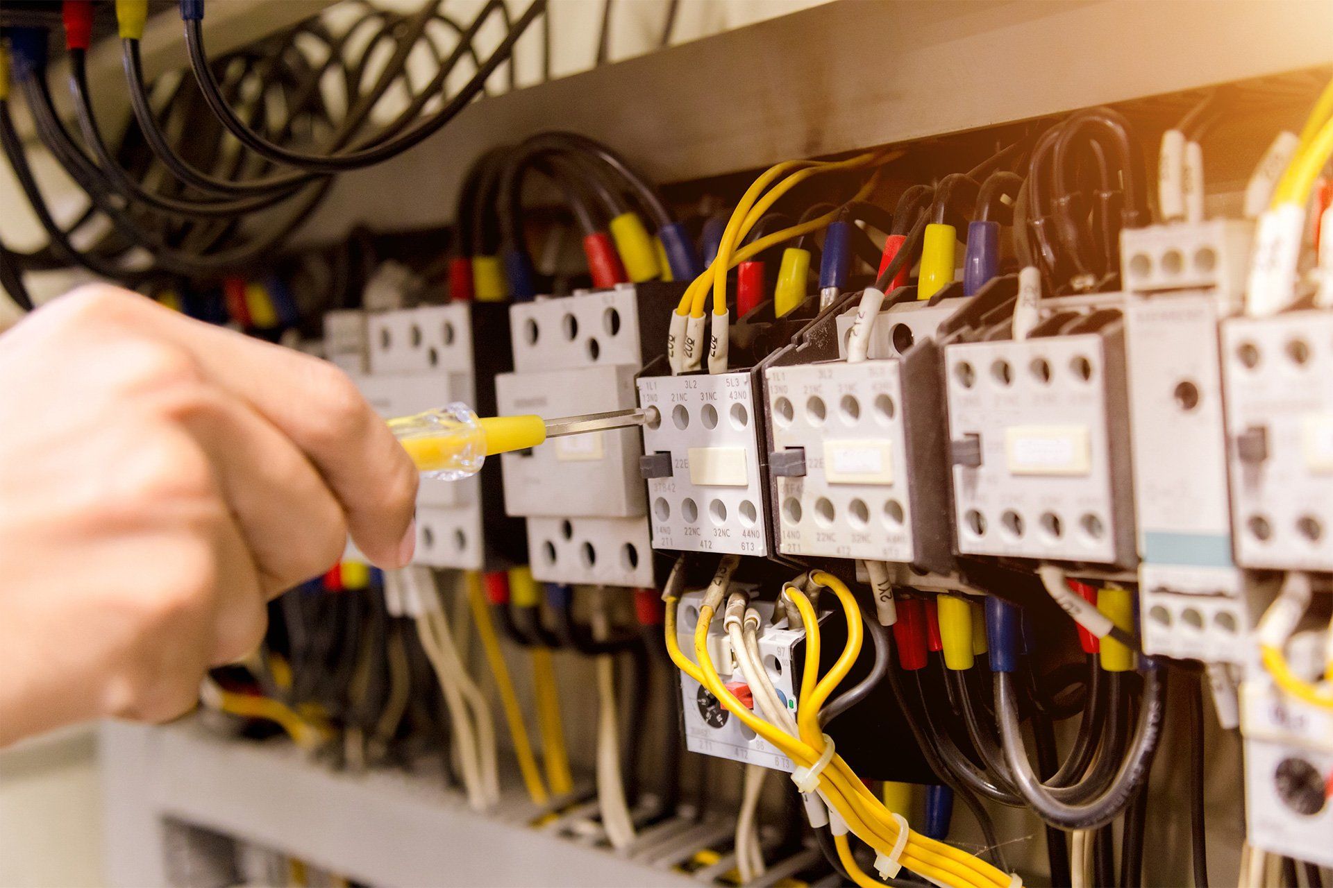 Hand connecting a yellow cable to an electrical control panel with relays and wiring