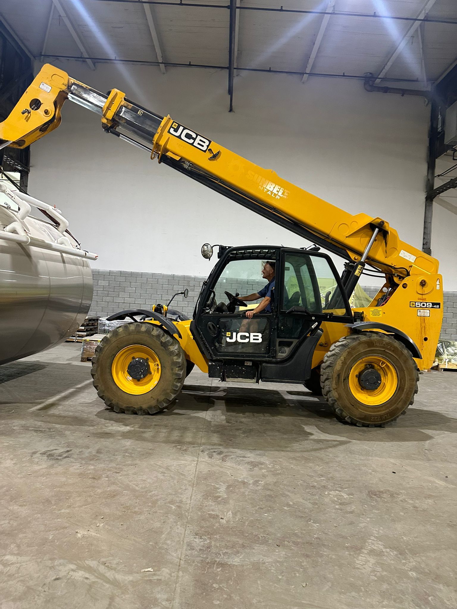 Chariot télescopique JCB jaune soulevant un bateau à l'intérieur d'un entrepôt.