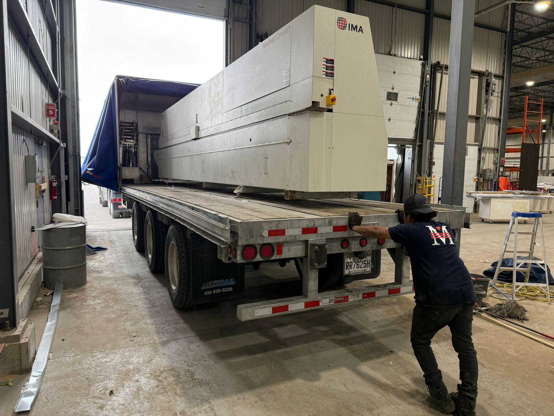 Un ouvrier pousse une grande machine blanche d'un camion à plateau à l'intérieur d'un entrepôt.