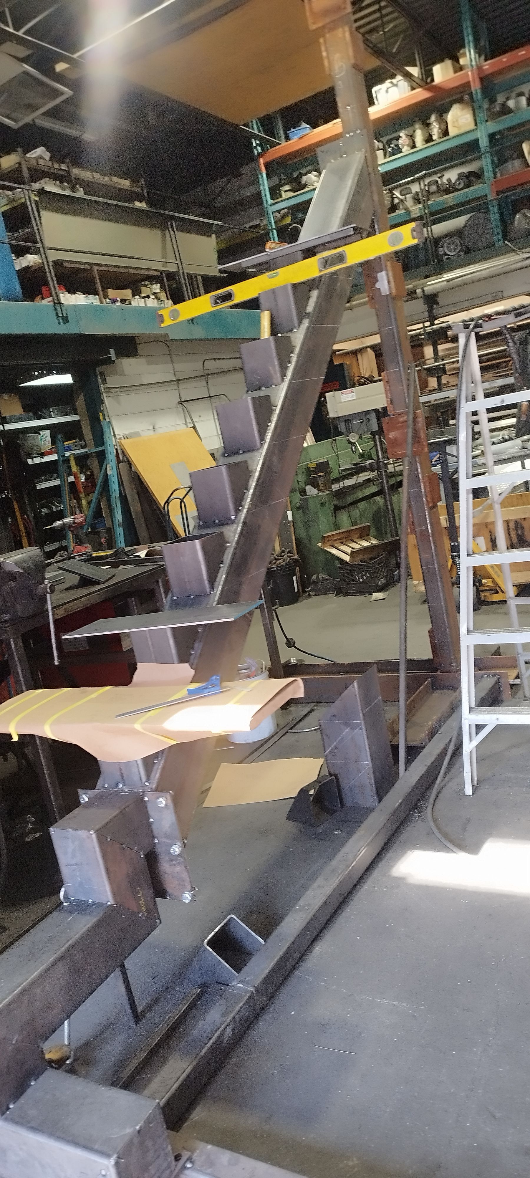 Structure d'escalier métallique dans un atelier avec outils et matériaux visibles en arrière-plan.
