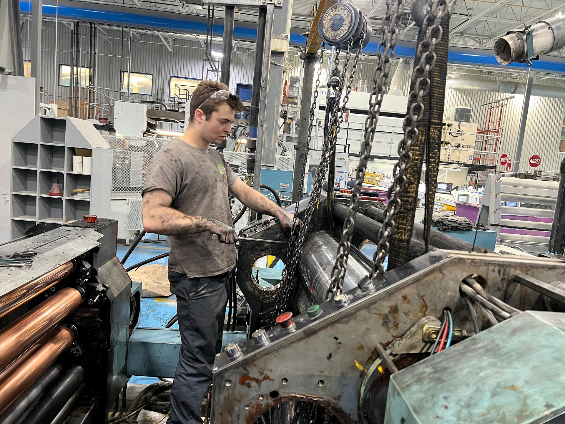 Un homme travaille sur des machines dans une usine. Ses vêtements et ses mains sont sales.