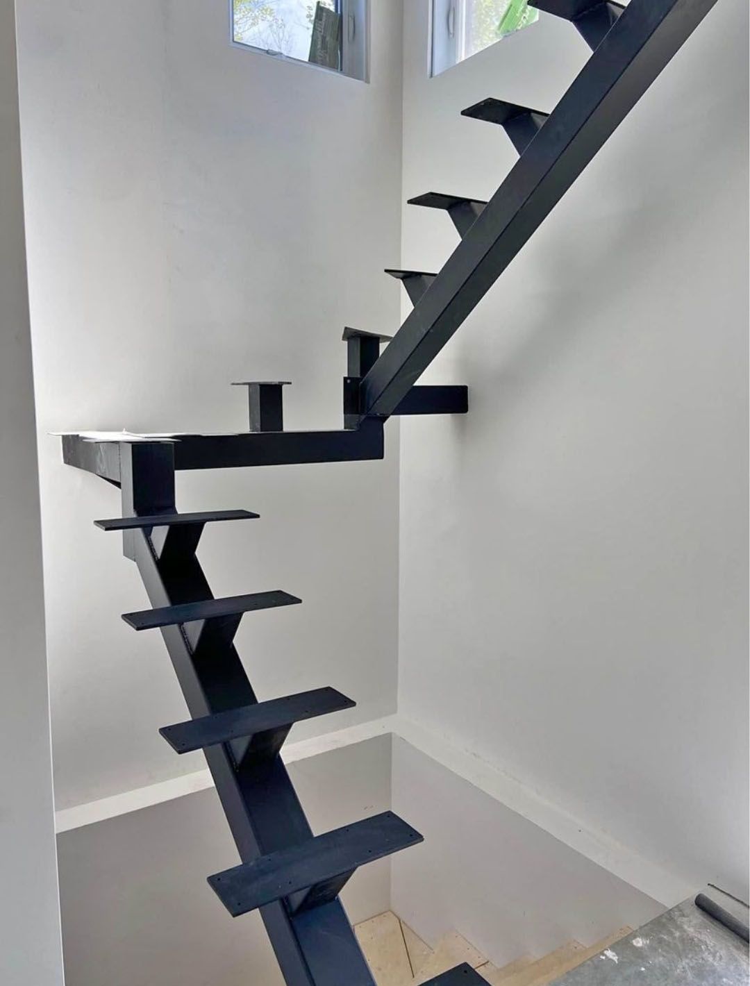 Escalier en métal noir contre un mur blanc, menant à un deuxième étage.
