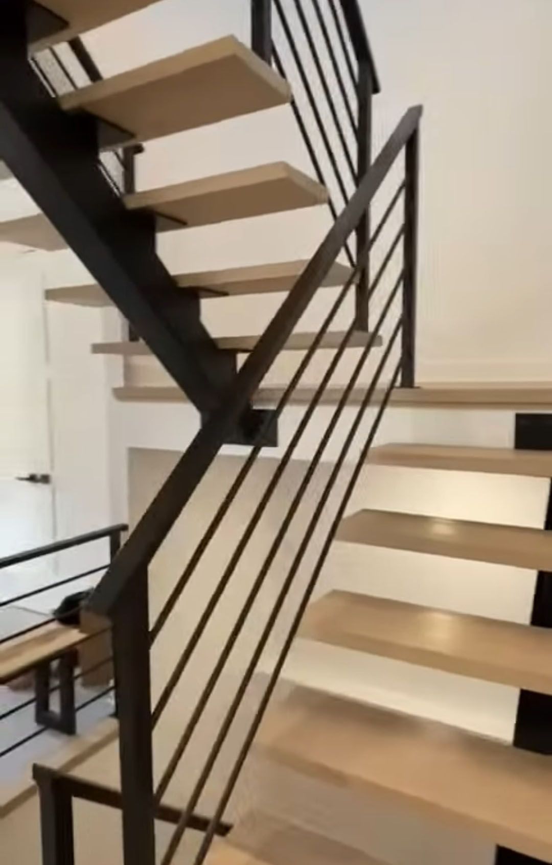 Escalier moderne avec marches en bois clair, rampe en métal noir et murs blancs.