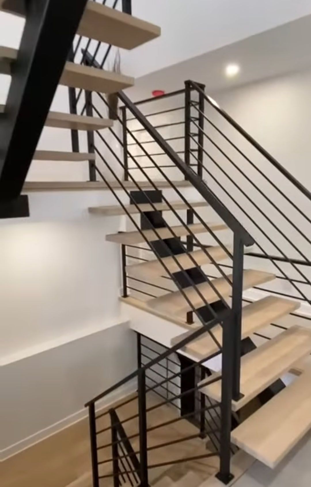 Escalier moderne avec marches en bois clair, rampes en métal noir, murs blancs.