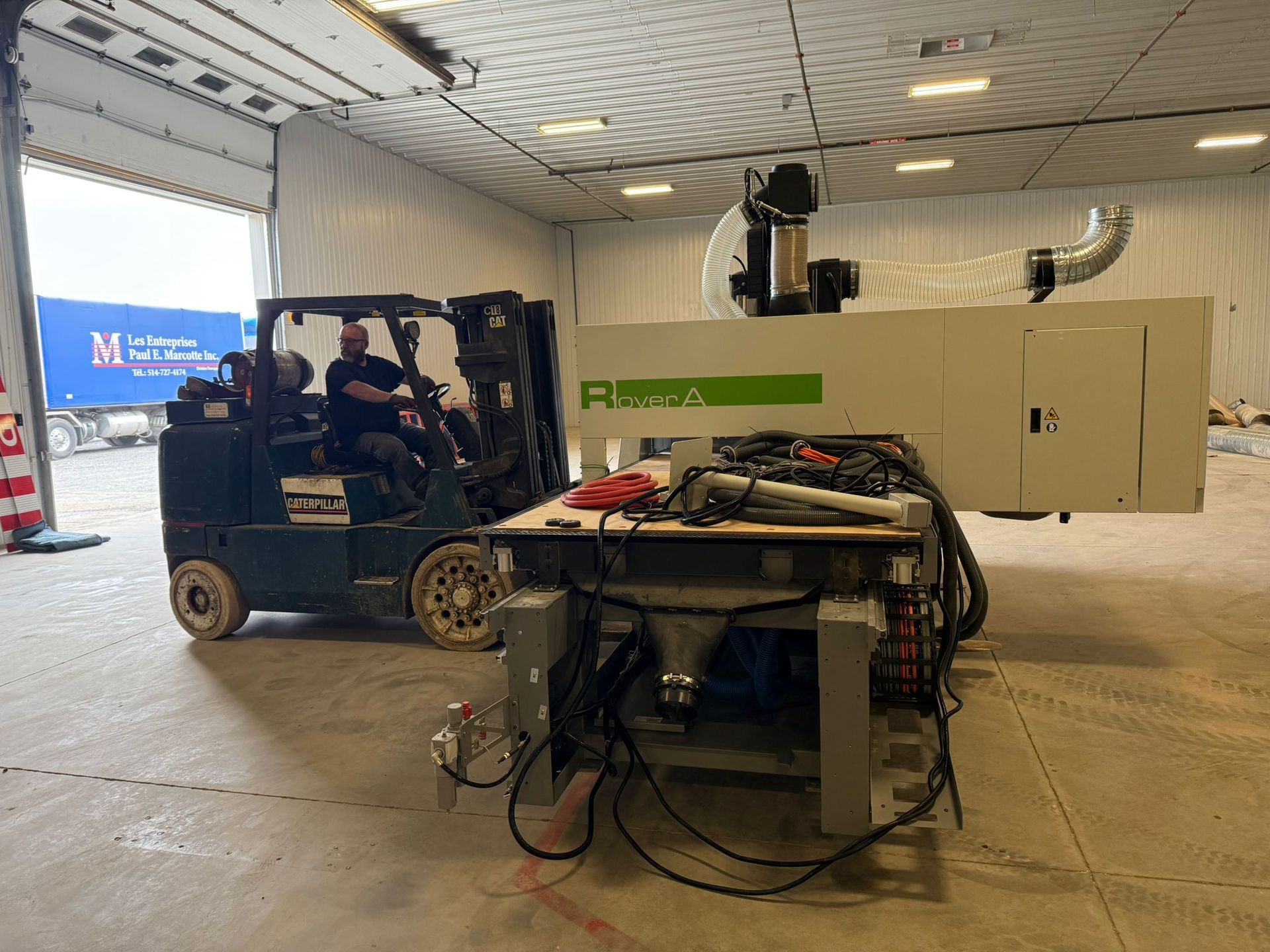 Chariot élévateur déplaçant des machines à l'intérieur d'un entrepôt, avec une personne au volant et une autre sur le siège passager.