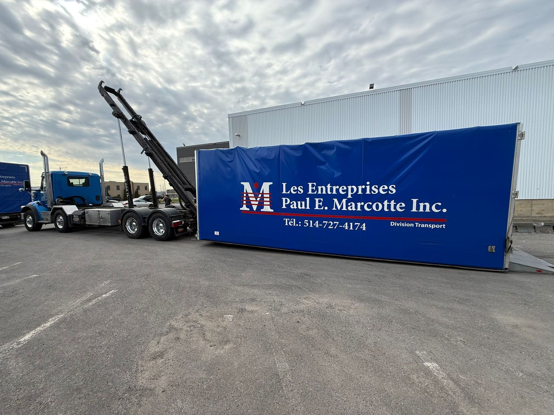 Camion bleu transportant un grand conteneur bleu. « Les Entreprises Paul P. Marcotte Inc. » est inscrit sur le côté.