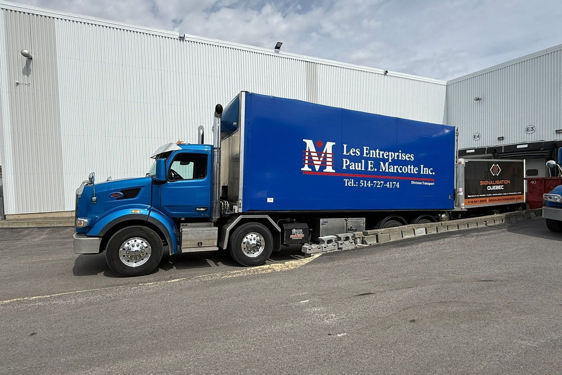Camion bleu avec une remorque réfrigérée devant un bâtiment.