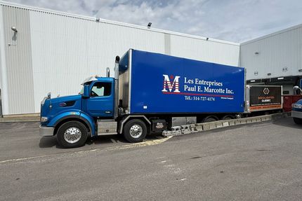 Camion bleu avec une remorque réfrigérée devant un bâtiment.