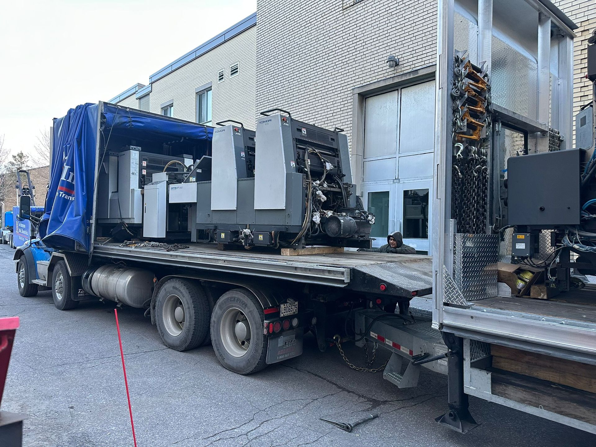 Une grande presse à imprimer est fixée sur un camion à plateau, prête à être transportée.