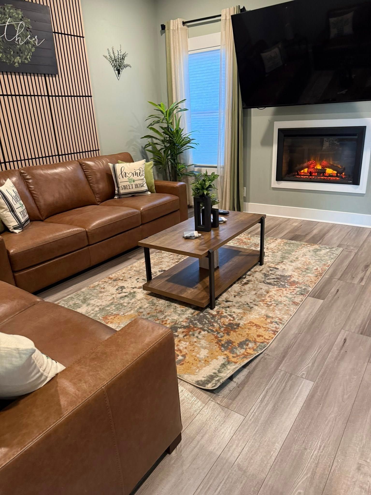 Modern living room with brown leather sofas, fireplace, coffee table, rug, and large wall-mounted TV
