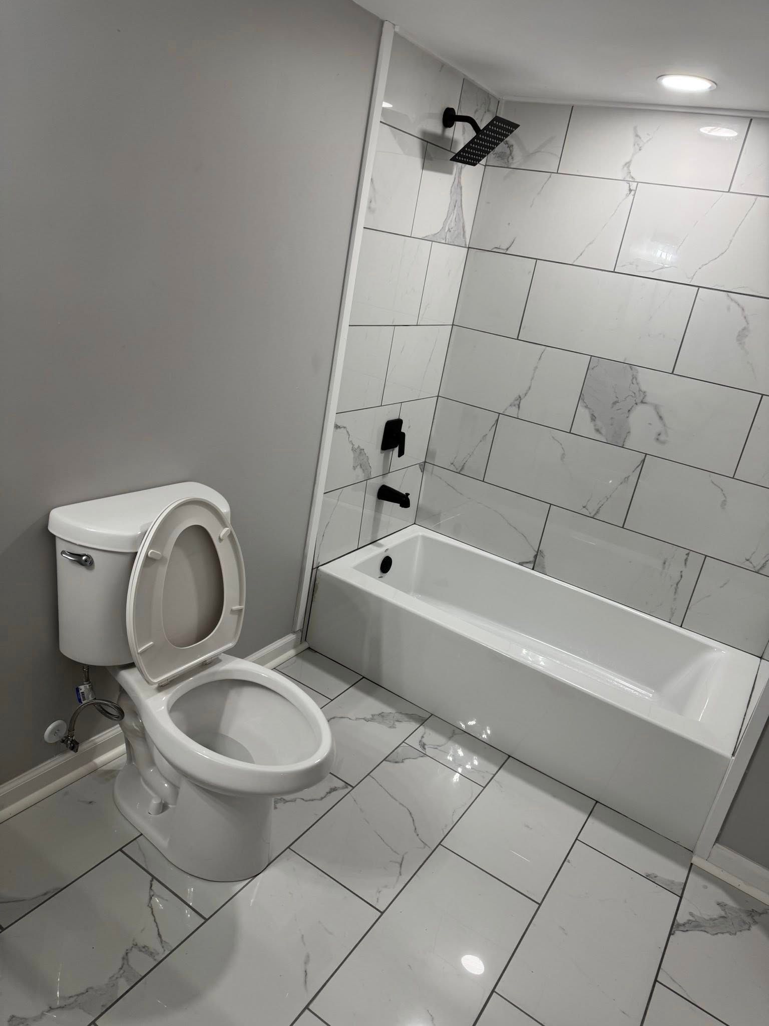 Small white bathroom with toilet, bathtub, and tiled floor and walls.
