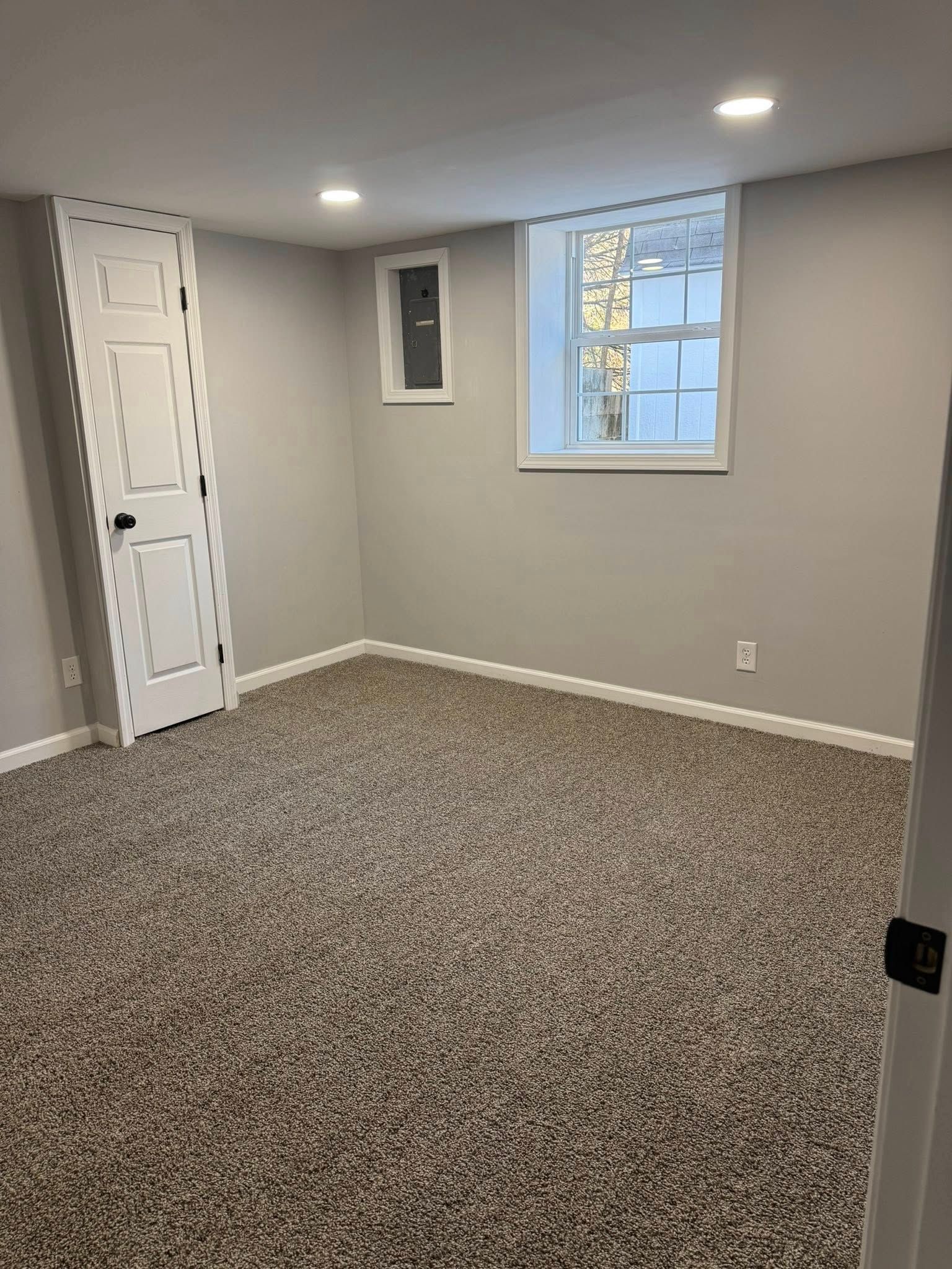 Empty carpeted room with gray walls, recessed lights, and a small window near a white closet door.