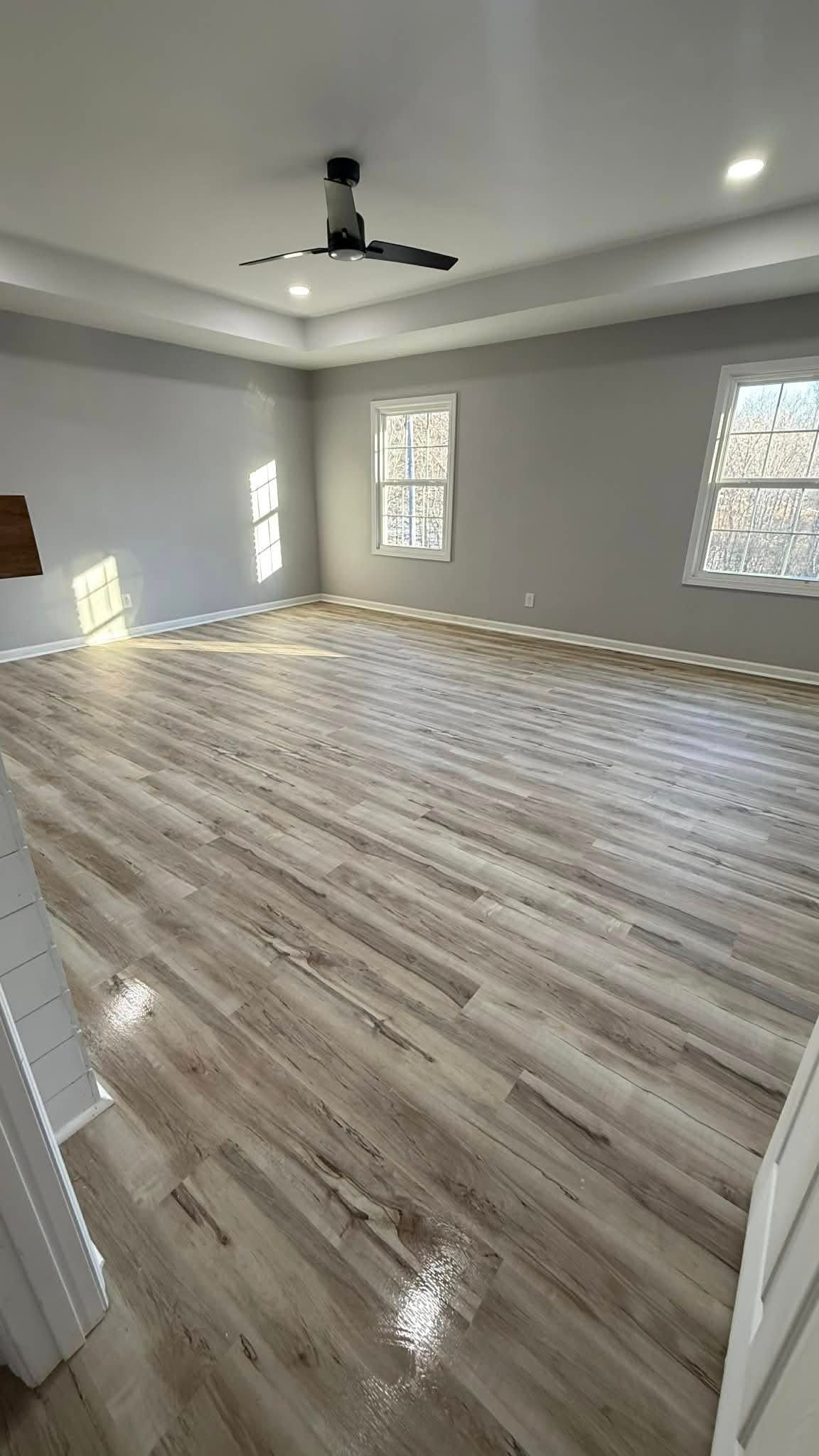 Empty modern room with glossy wood-look floors, gray walls, recessed lights, and large windows.